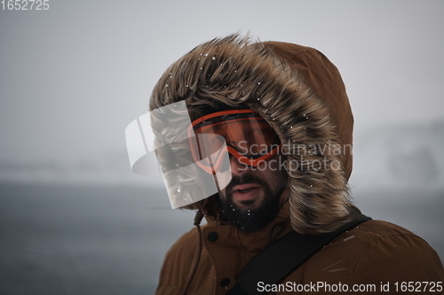 Image of man at winter in stormy weather wearing warm fur jacket