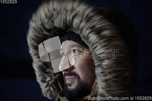 Image of man at winter in stormy weather night wearing warm fur jacket