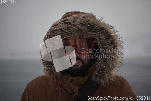 Image of man at winter in stormy weather wearing warm fur jacket