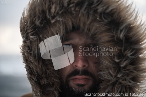 Image of man at winter in stormy weather wearing warm fur jacket