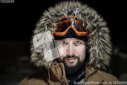 Image of man at winter in stormy weather night wearing warm fur jacket