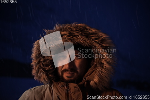 Image of man at winter in stormy weather night wearing warm fur jacket