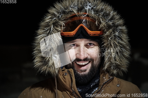 Image of man at winter in stormy weather night wearing warm fur jacket