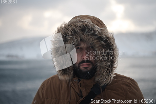 Image of man at winter in stormy weather wearing warm fur jacket