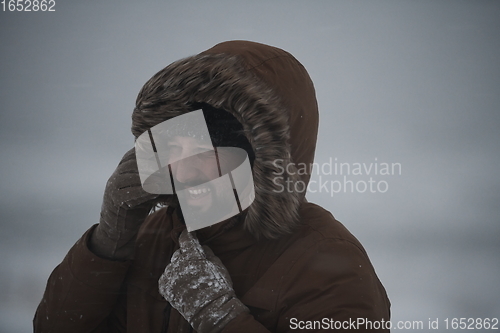 Image of man at winter in stormy weather wearing warm fur jacket