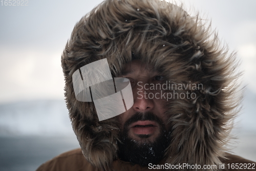 Image of man at winter in stormy weather wearing warm fur jacket