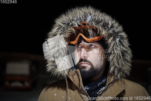 Image of man at winter in stormy weather night wearing warm fur jacket