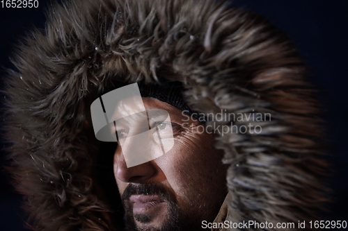 Image of man at winter in stormy weather night wearing warm fur jacket