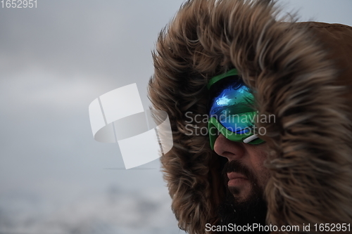 Image of man at winter in stormy weather wearing warm fur jacket