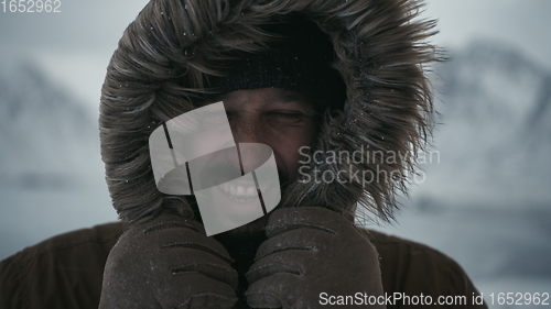 Image of man at winter in stormy weather wearing warm fur jacket