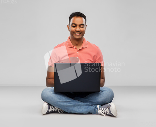 Image of happy indian man with laptop computer on floor