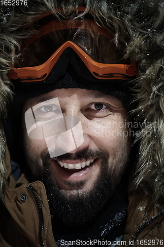 Image of man at winter in stormy weather night wearing warm fur jacket