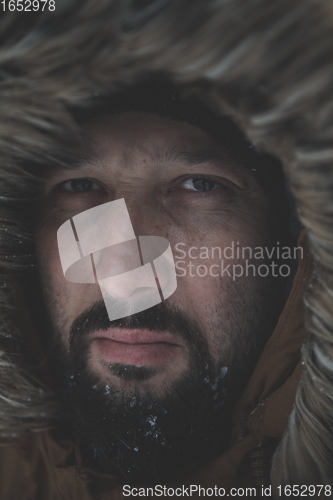 Image of man at winter in stormy weather wearing warm fur jacket