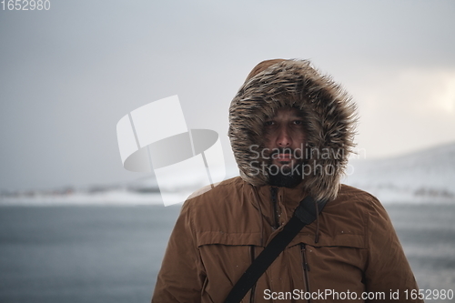 Image of man at winter in stormy weather wearing warm fur jacket