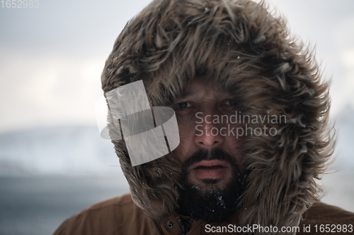 Image of man at winter in stormy weather wearing warm fur jacket