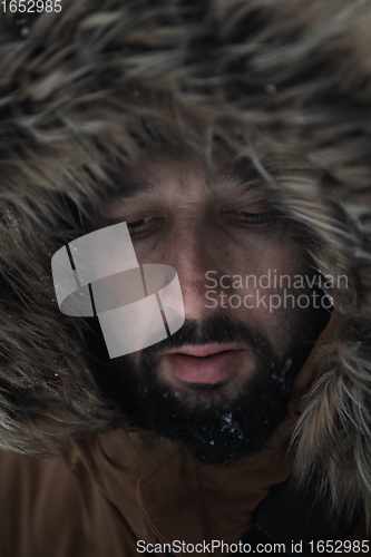 Image of man at winter in stormy weather wearing warm fur jacket