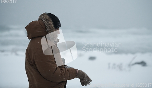 Image of man at winter in stormy weather wearing warm fur jacket