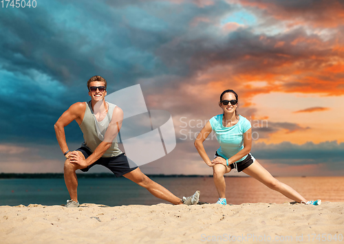 Image of smiling couple stretching legs on beach