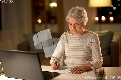 Image of senior woman writing to notebook at home at night