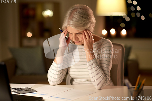 Image of senior woman filling tax form at home in evening