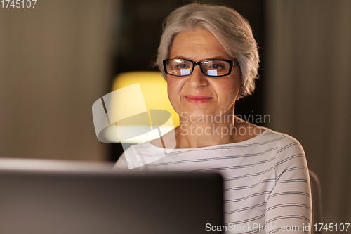 Image of happy senior woman with laptop at home in evening