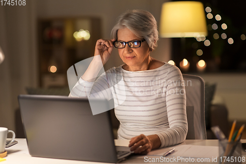 Image of senior woman with laptop working at home at night