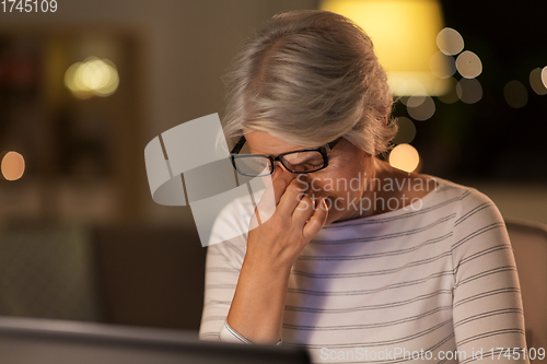 Image of tired senior woman with laptop at home at night