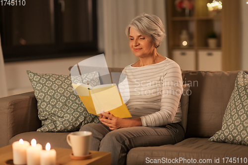 Image of happy senior woman reading book at home in evening