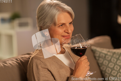 Image of senior woman drinking red wine at home in evening