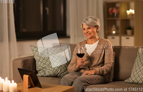 Image of senior woman with tablet pc drinking wine at home