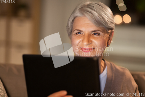 Image of happy senior woman with tablet pc at home at night