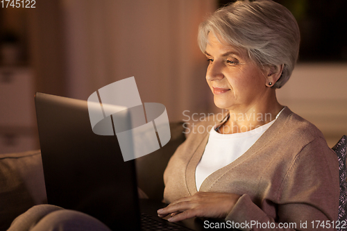 Image of happy senior woman with laptop at home at night