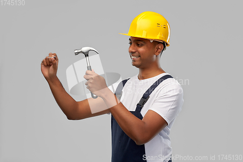 Image of happy indian worker or builder hammering nail