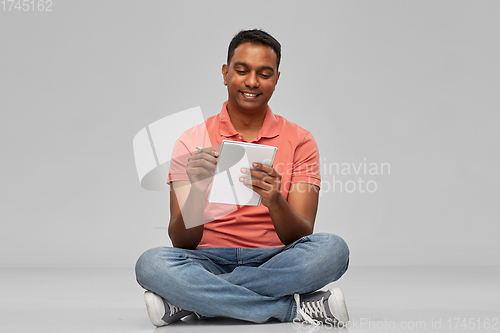 Image of indian man in polo shirt writing to notebook