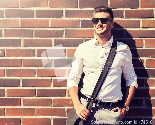 Image of young man in sunglasses with bag over brickwall