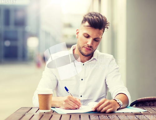 Image of man with coffee and folder writing at city cafe