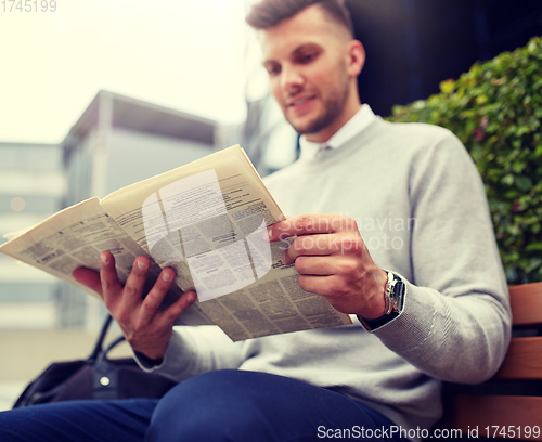 Image of man reading newspaper on city street bench