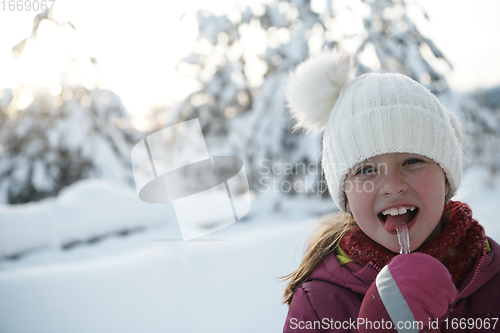 Image of cute little girl while eating icicle on beautiful winter day