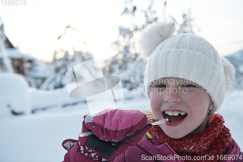 Image of cute little girl while eating icicle on beautiful winter day