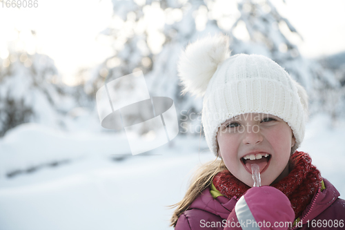 Image of cute little girl while eating icicle on beautiful winter day