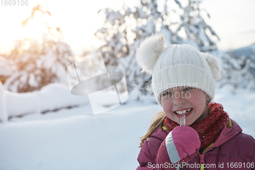 Image of cute little girl while eating icicle on beautiful winter day