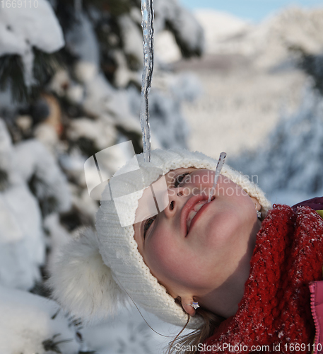 Image of cute little girl while eating icicle on beautiful winter day