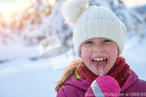 Image of cute little girl while eating icicle on beautiful winter day