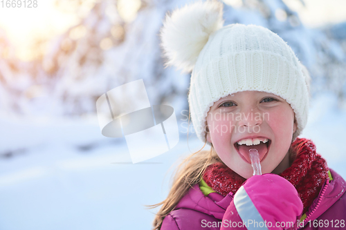 Image of cute little girl while eating icicle on beautiful winter day