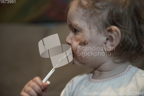 Image of baby girl eating her chocolate desert with a spoon and making a mess