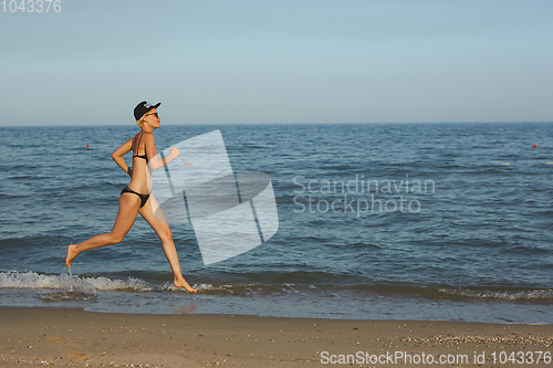 Image of Active sporty woman run along ocean surf by water pool to keep fit and health. Sunset black sand beach background with sun. Woman fitness, jogging workout and sport activity on summer family holiday.