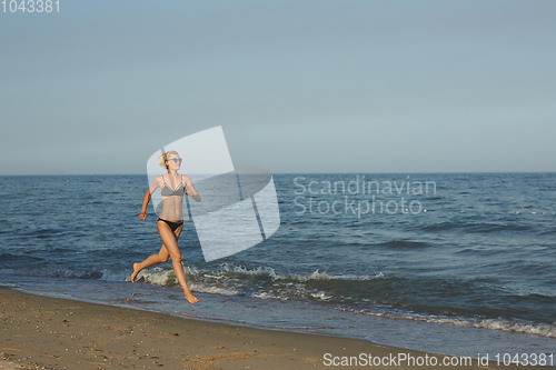 Image of Side view of a woman running on the beach with the horizon and sea in the background
