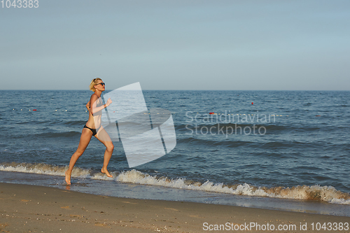 Image of Side view of a woman running on the beach with the horizon and sea in the background