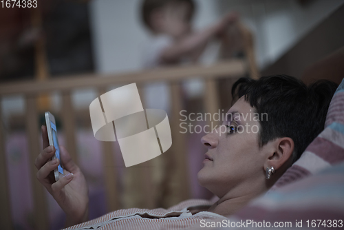 Image of mother is using smarphone in bed while baby sleeping