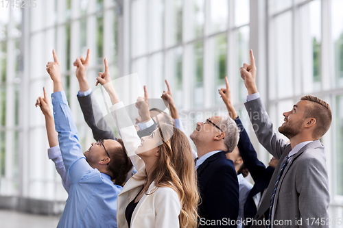 Image of happy business team pointing finger up at office